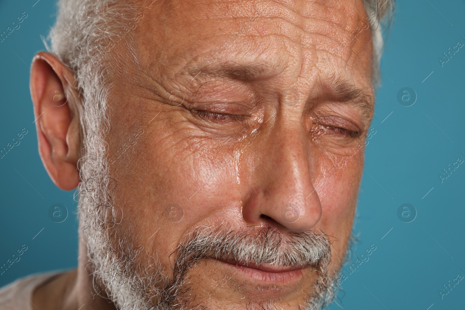 Photo of Sad senior man crying on light blue background, closeup