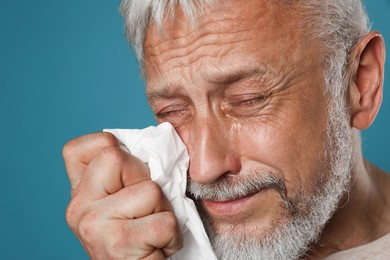 Photo of Sad senior man crying on light blue background, closeup