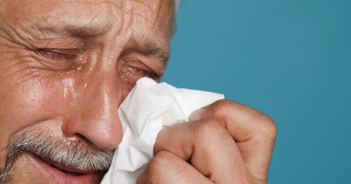 Photo of Sad senior man crying on light blue background, closeup