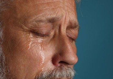 Photo of Sad senior man crying on blue background, closeup. Space for text