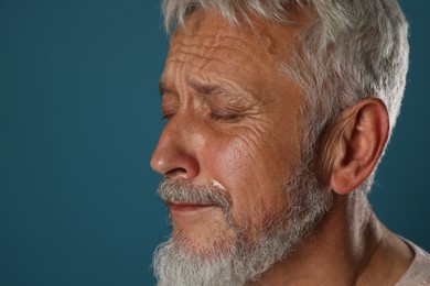 Photo of Sad senior man crying on blue background, closeup