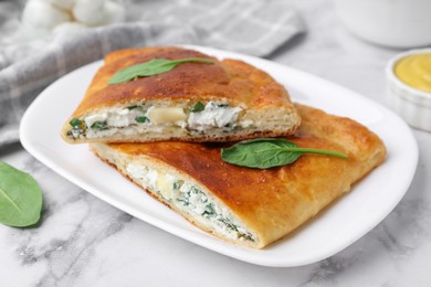 Photo of Pieces of tasty calzone with cheese and basil on white marble table, closeup