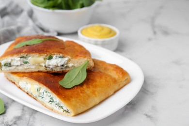 Photo of Pieces of tasty calzone with basil, cheese and sauce on white marble table, closeup. Space for text