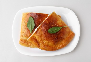 Photo of Pieces of tasty calzone with cheese and basil on white background, top view