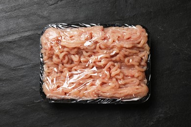 Photo of Plastic pack with fresh minced meat on black textured table, top view