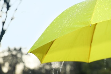 Photo of Open yellow umbrella under pouring rain outdoors, closeup. Space for text