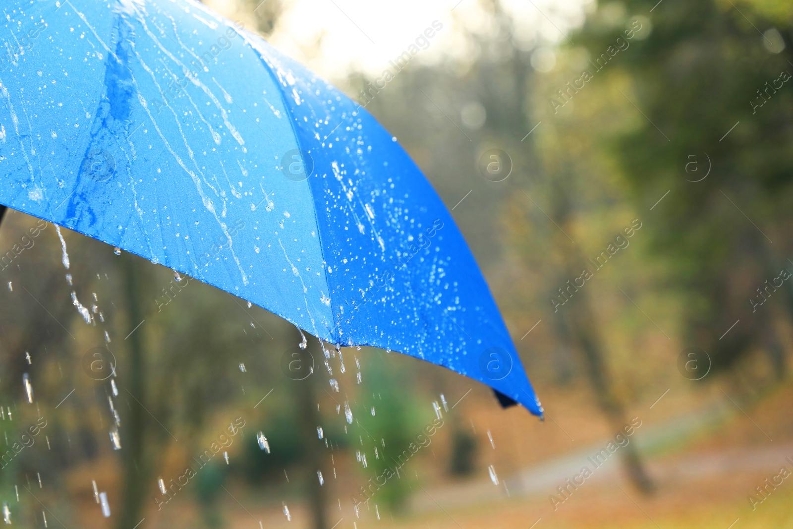 Photo of Open blue umbrella under pouring rain outdoors, closeup. Space for text