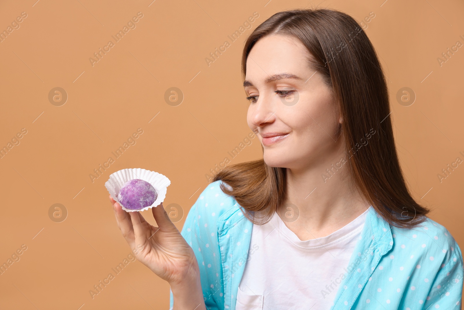 Photo of Woman with tasty mochi on light brown background. Space for text