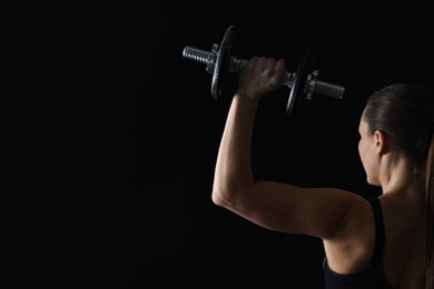 Photo of Woman training with barbells on black background, back view. Space for text