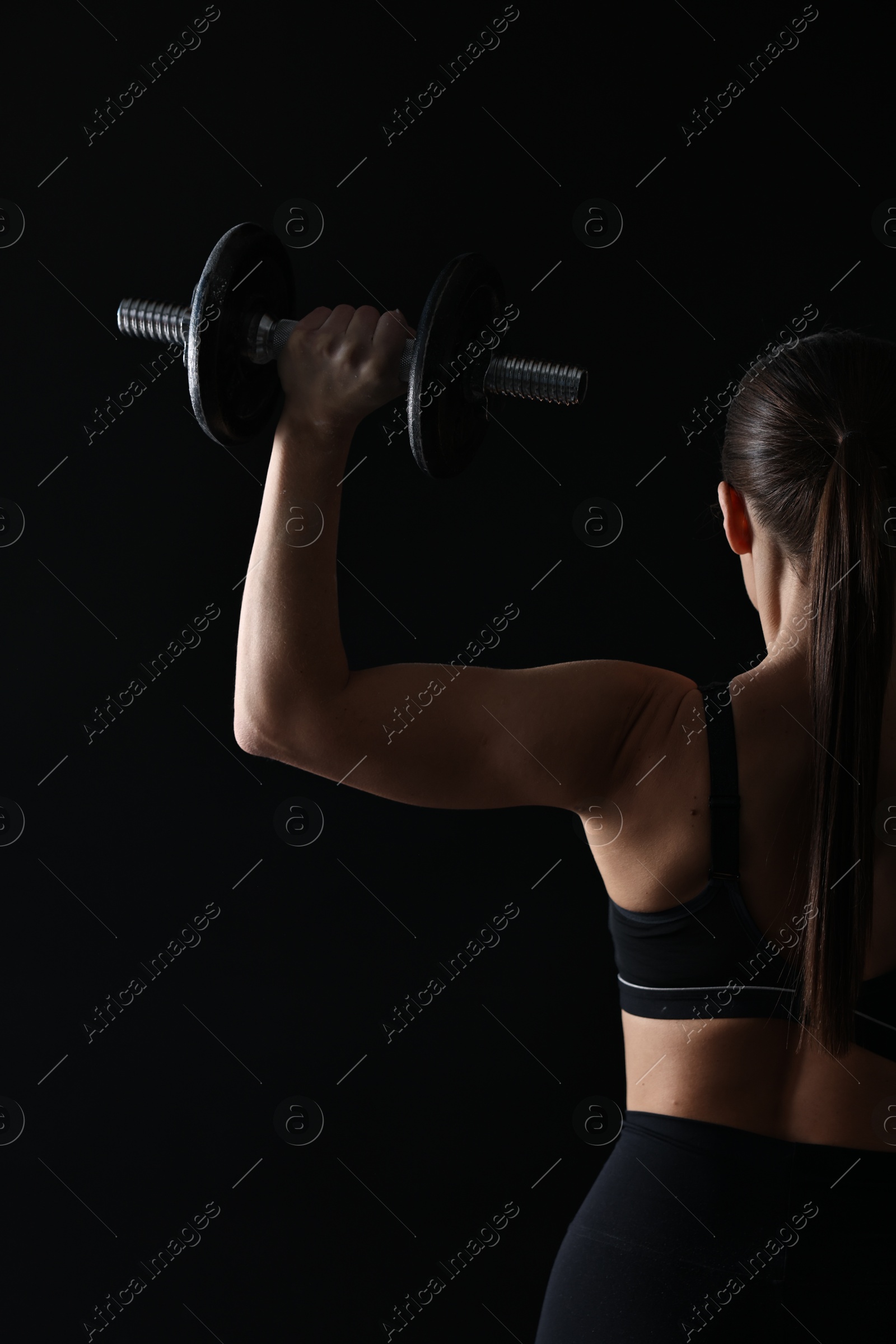 Photo of Woman training with barbells on black background, back view