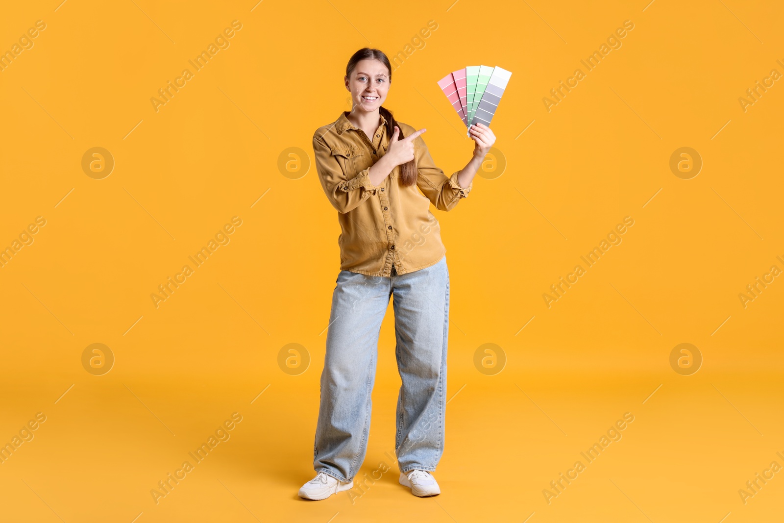 Photo of Woman with paint color selection chart on orange background