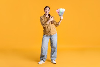 Photo of Woman with paint color selection chart on orange background