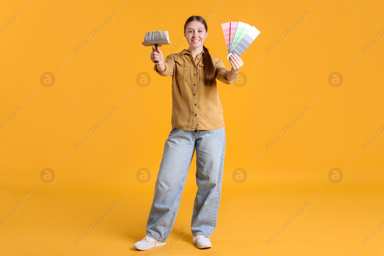 Photo of Woman with paintbrush and color selection chart on orange background