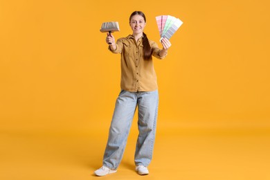 Photo of Woman with paintbrush and color selection chart on orange background