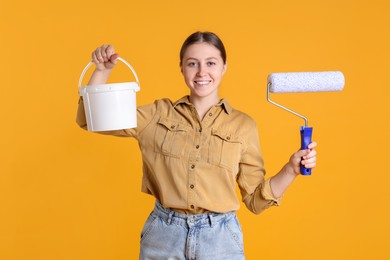 Photo of Woman with roller and bucket of paint on orange background