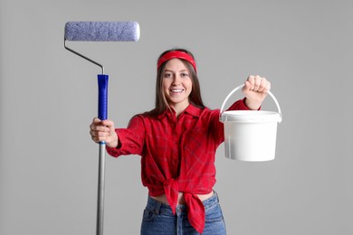 Photo of Woman with roller and bucket of paint on light grey background