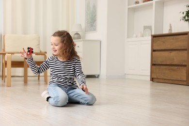 Little girl playing with toy car on floor at home, space for text