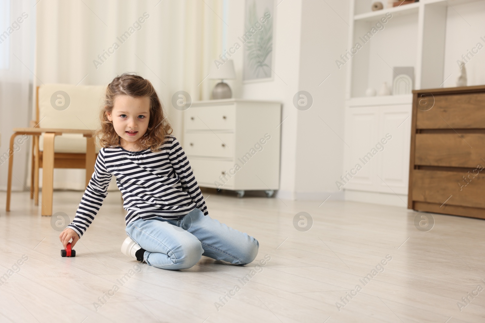 Photo of Little girl playing with toy car on floor at home, space for text