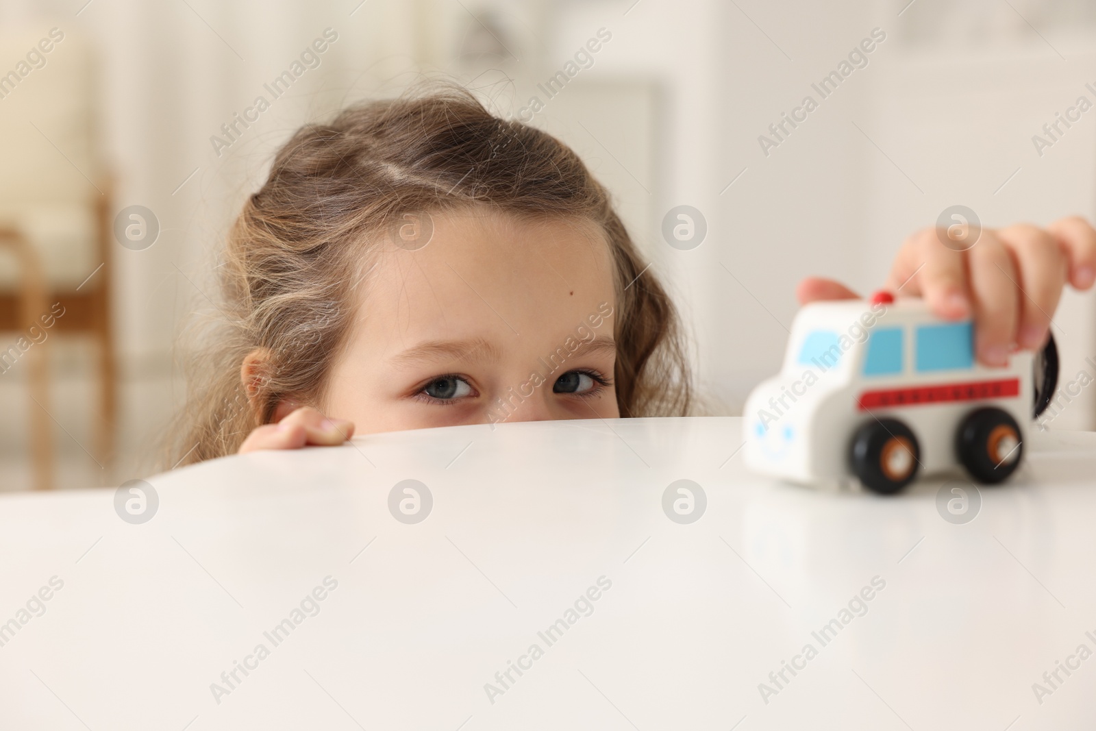 Photo of Little girl playing with toy car at white table indoors, closeup