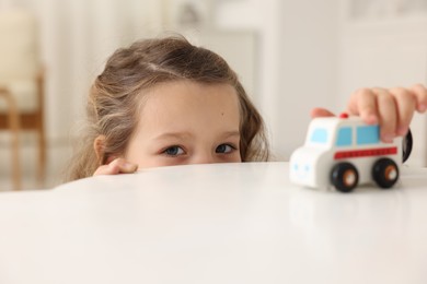 Photo of Little girl playing with toy car at white table indoors, closeup