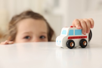 Photo of Little girl playing with toy car at white table indoors, selective focus