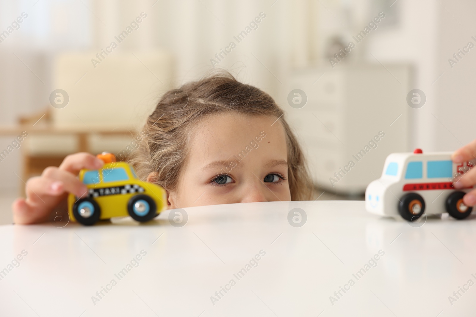 Photo of Little girl playing with toy cars at white table indoors, closeup