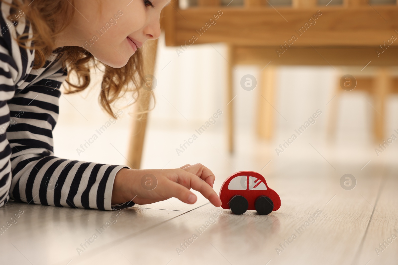 Photo of Little girl playing with toy car on floor at home, closeup. Space for text