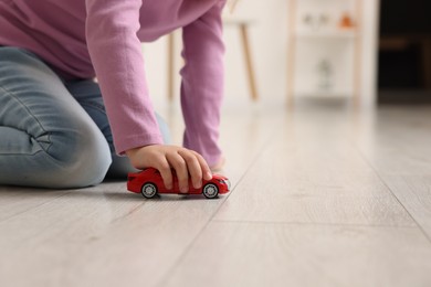 Photo of Little girl playing with toy car on floor at home, closeup. Space for text