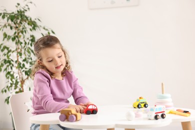 Photo of Little girl playing with toy cars at white table indoors, space for text