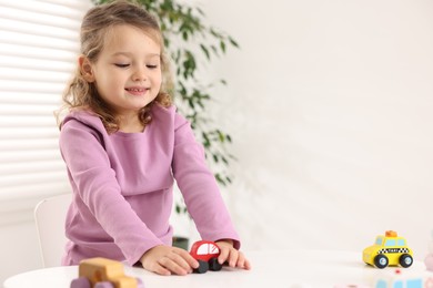 Photo of Little girl playing with toy cars at white table indoors, space for text