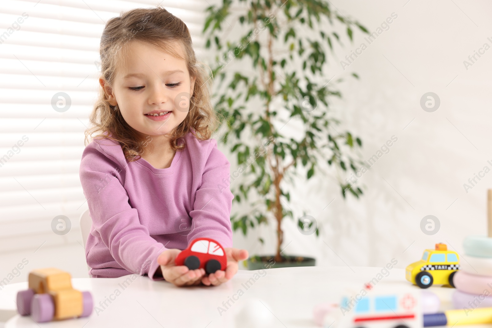 Photo of Little girl playing with toy cars at white table indoors, space for text