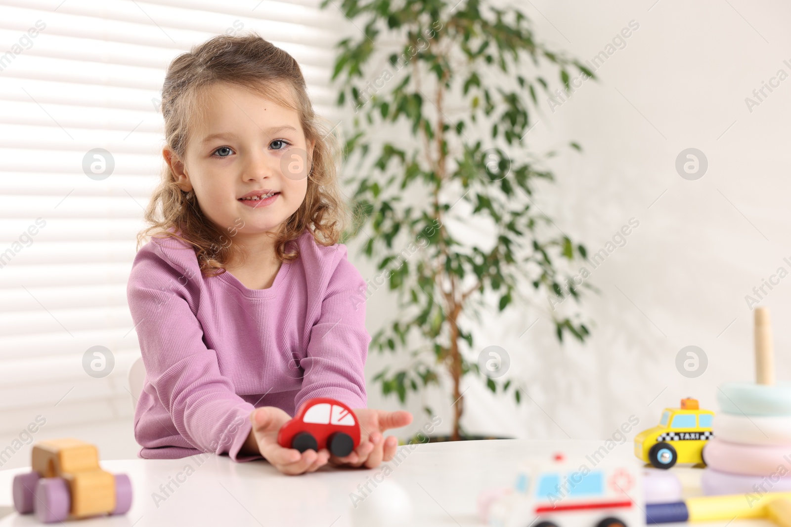 Photo of Little girl playing with toy cars at white table indoors, space for text