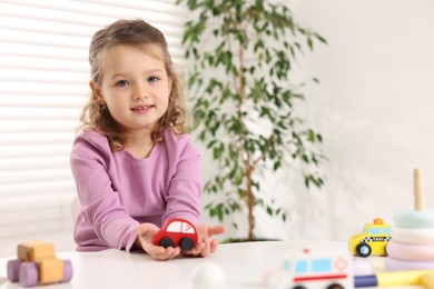 Photo of Little girl playing with toy cars at white table indoors, space for text