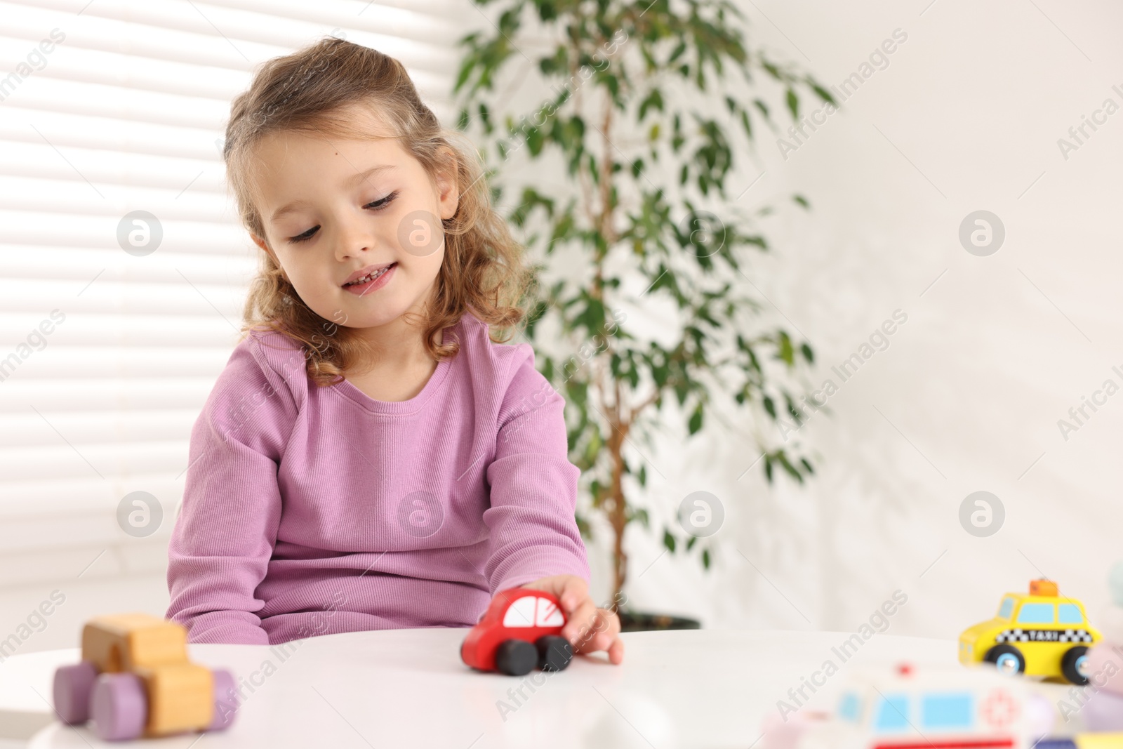 Photo of Little girl playing with toy cars at white table indoors, space for text