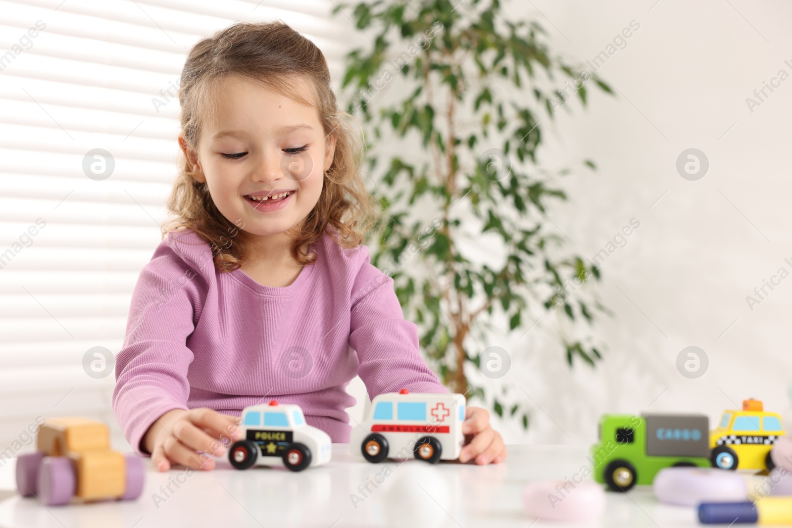 Photo of Little girl playing with toy cars at white table indoors, space for text