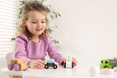 Photo of Little girl playing with toy cars at white table indoors, space for text