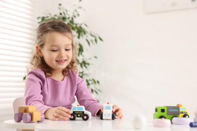 Photo of Little girl playing with toy cars at white table indoors, space for text