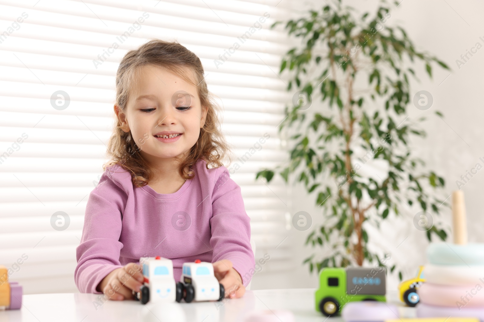 Photo of Little girl playing with toy cars at white table indoors, space for text