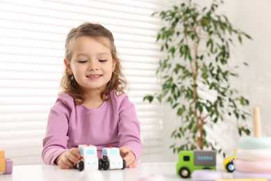 Photo of Little girl playing with toy cars at white table indoors, space for text