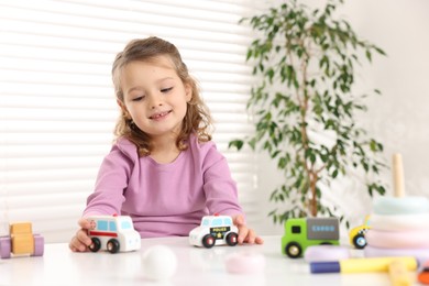 Photo of Little girl playing with toy cars at white table indoors, space for text