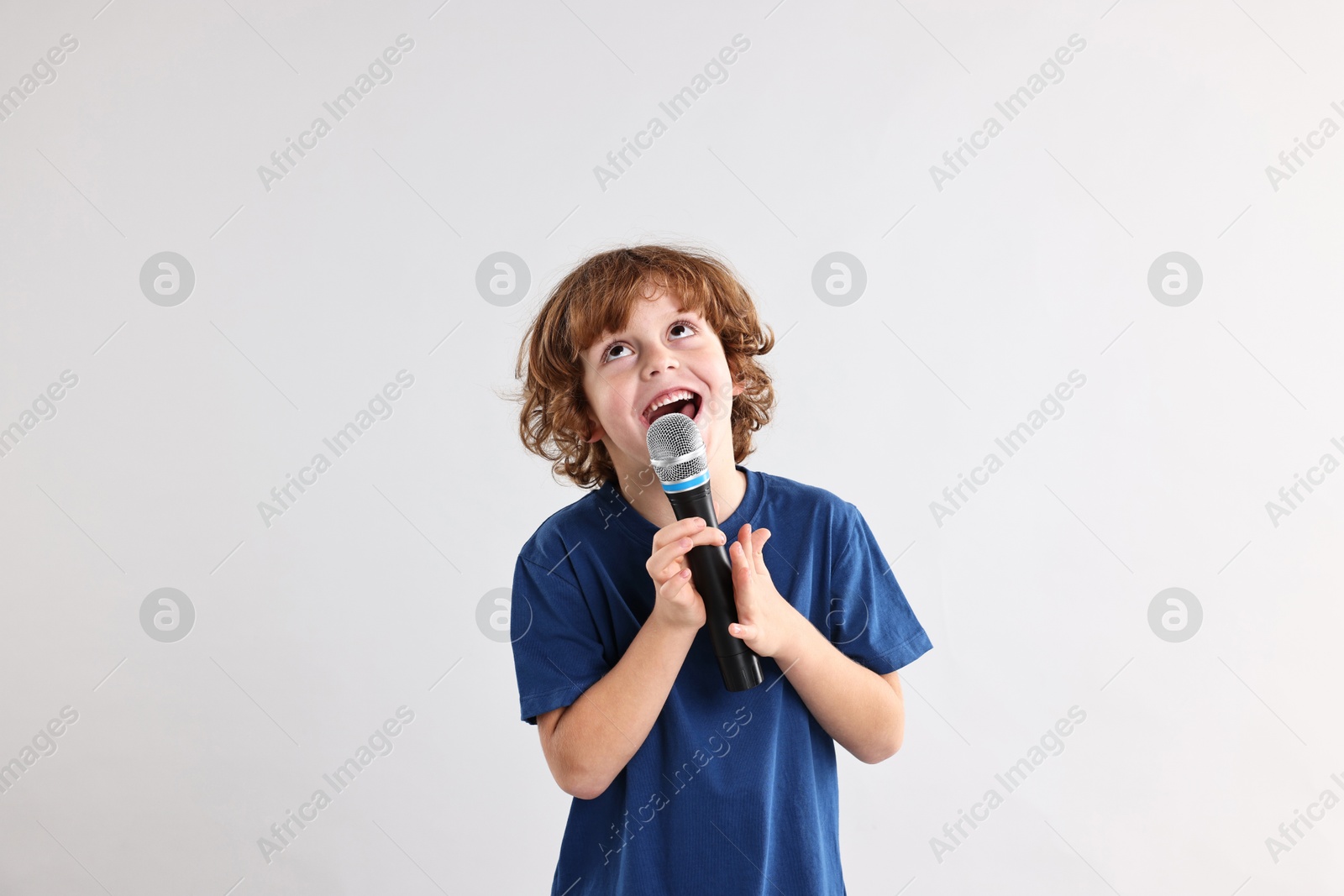 Photo of Little boy with microphone singing on light grey background