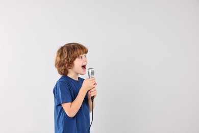 Photo of Little boy with microphone singing on light grey background, space for text