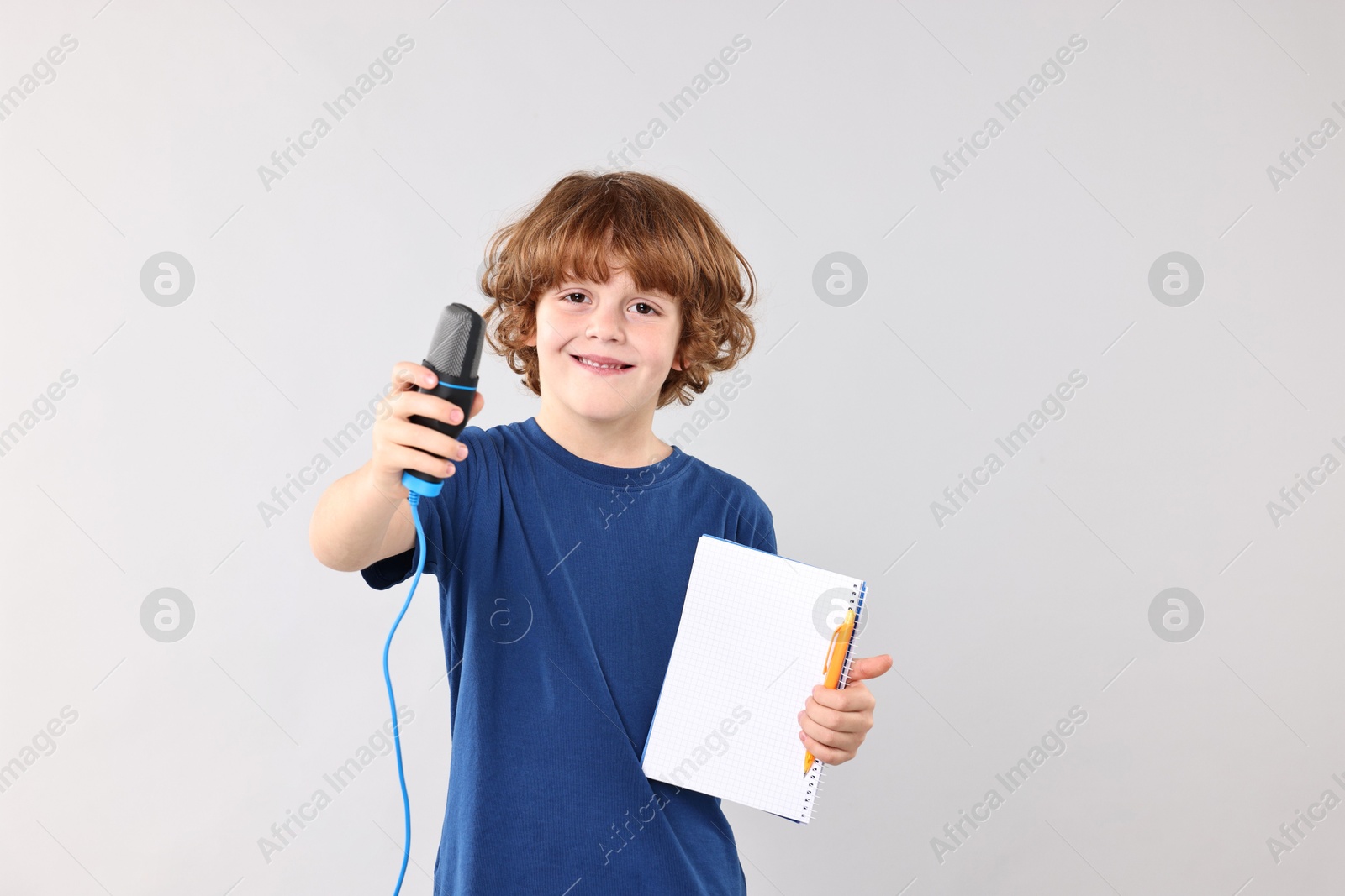 Photo of Little boy with microphone and notebook on light grey background