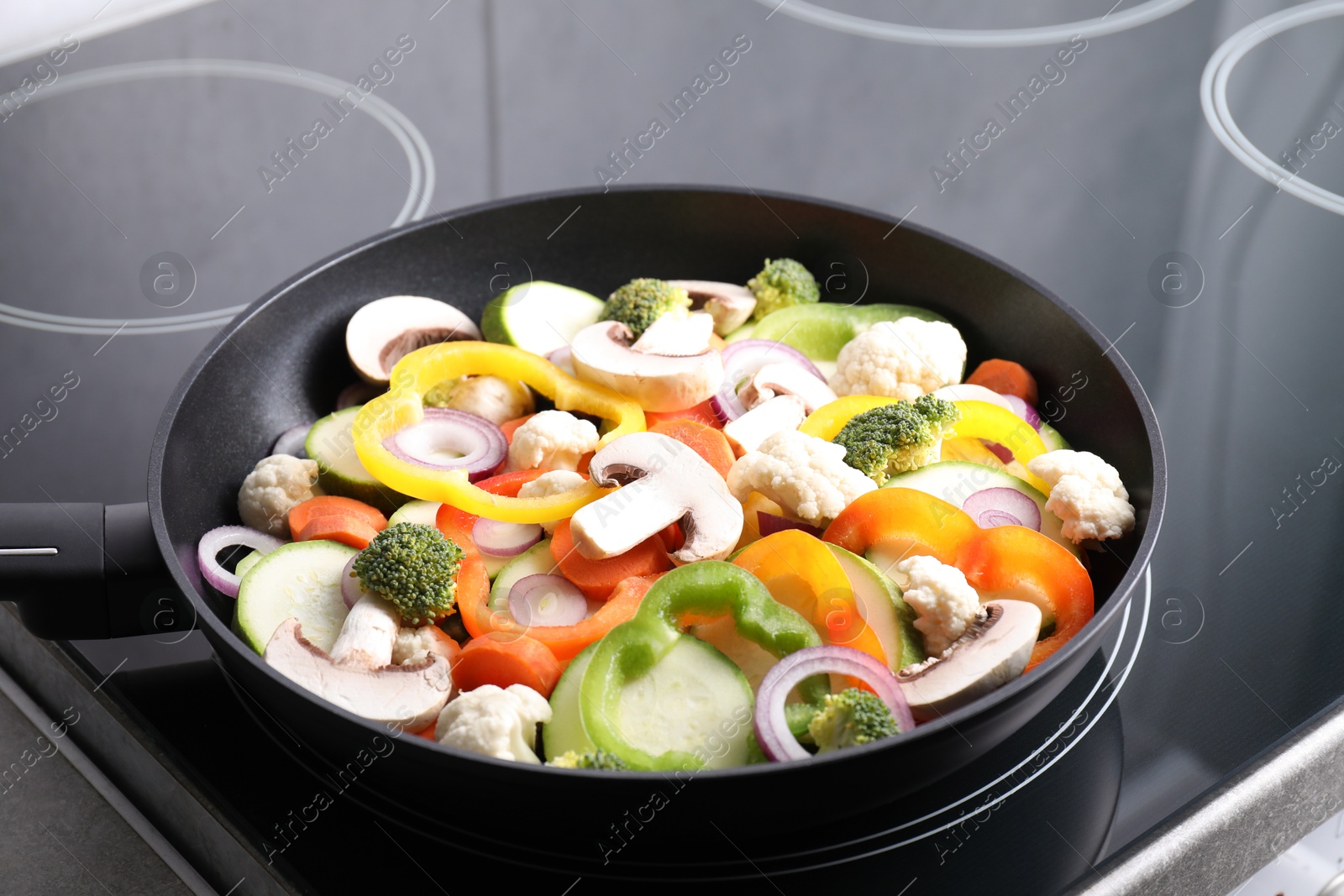 Photo of Frying pan with mix of vegetables and mushrooms on cooktop, closeup