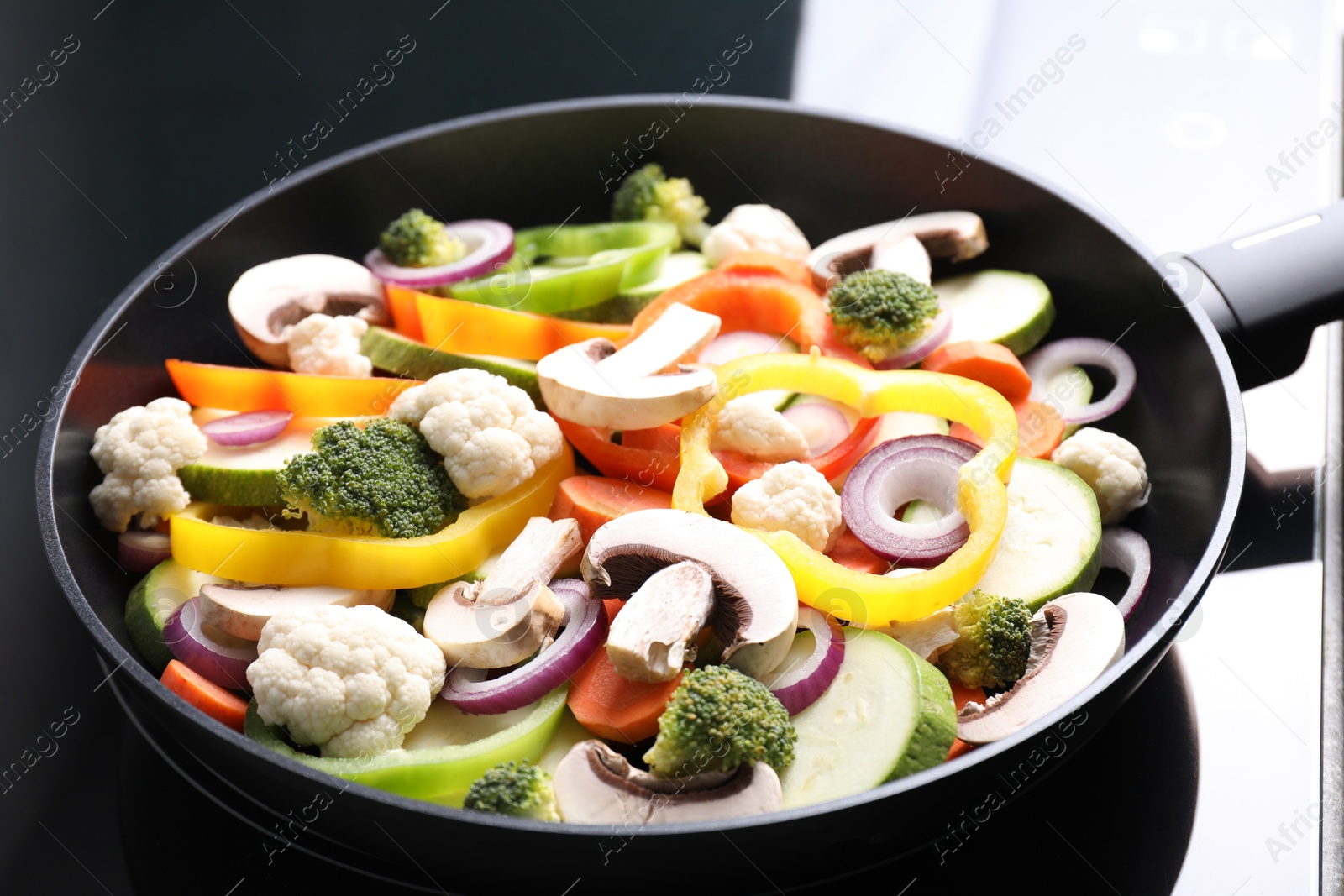 Photo of Frying pan with mix of vegetables and mushrooms on cooktop, closeup