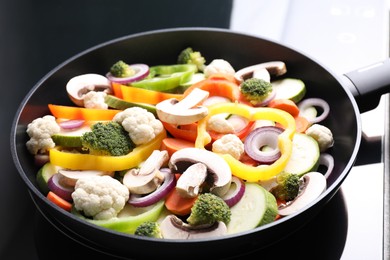 Photo of Frying pan with mix of vegetables and mushrooms on cooktop, closeup