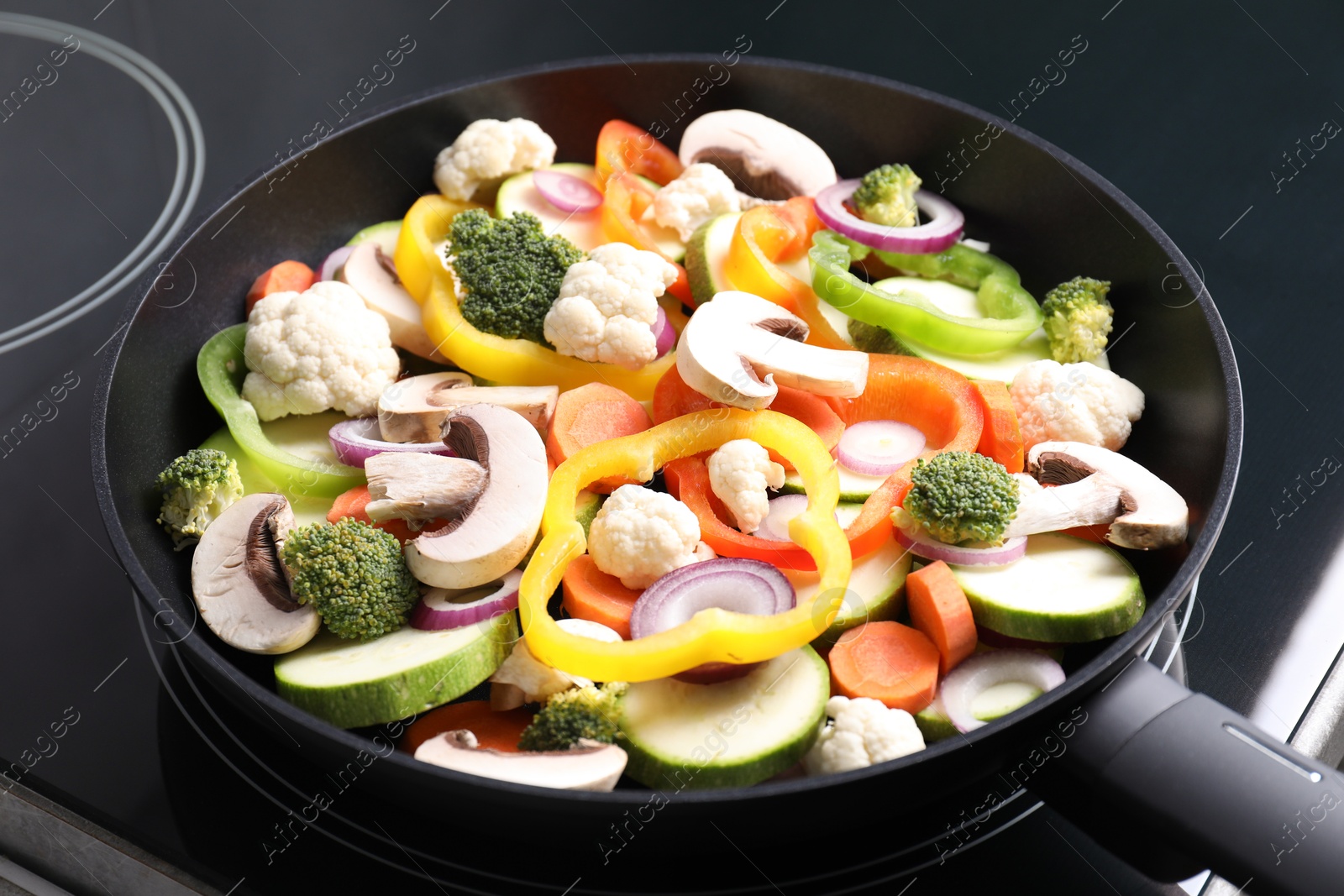 Photo of Frying pan with mix of vegetables and mushrooms on cooktop, closeup