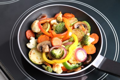 Photo of Frying pan with mix of vegetables and mushrooms on cooktop, closeup