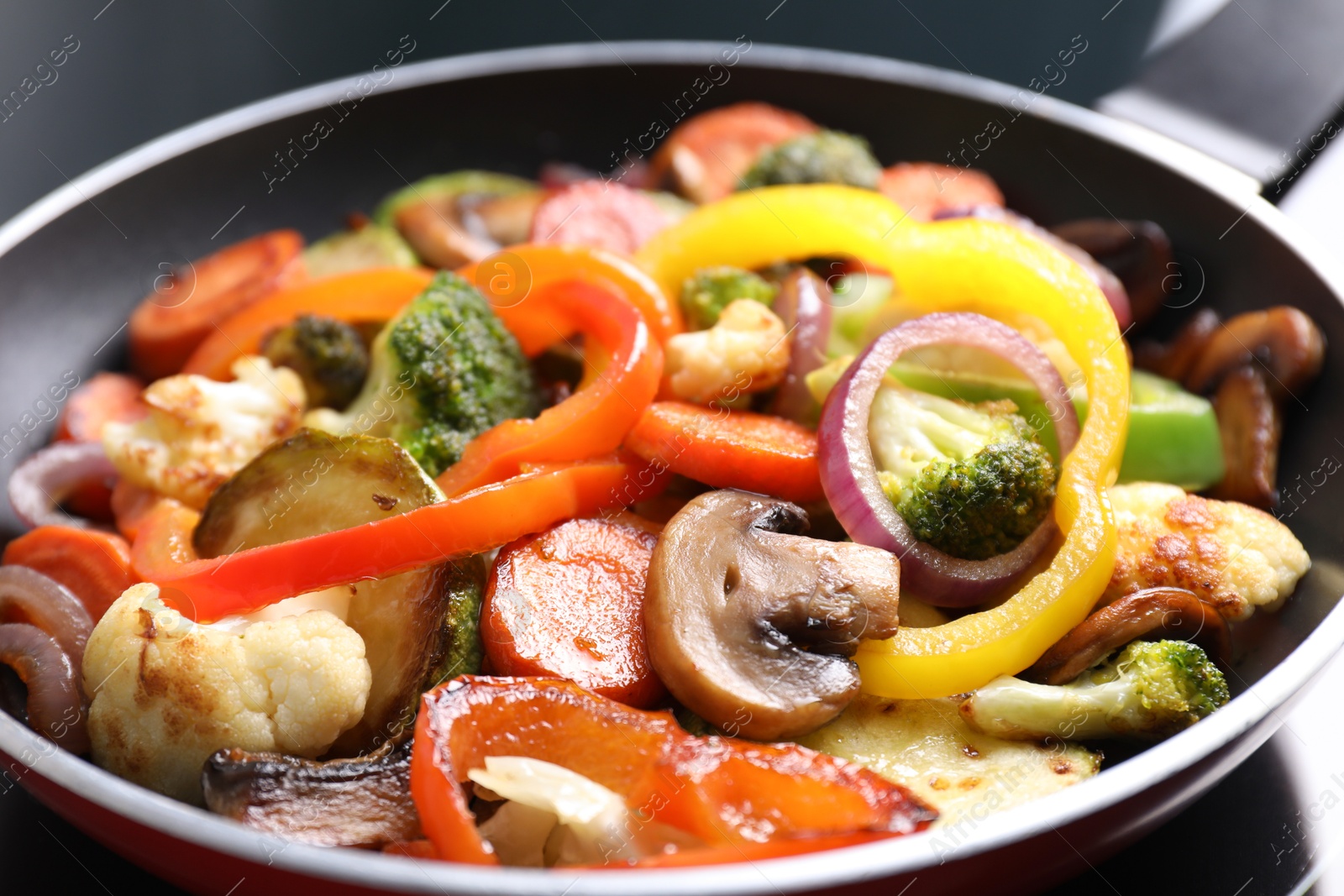 Photo of Frying pan with mix of vegetables and mushrooms on cooktop, closeup