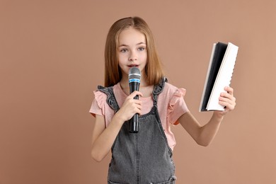 Photo of Little girl with microphone and notebook singing on light brown background